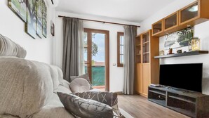 A living room with a sofa, a flat-screen TV, wooden cabinets, and a sliding glass door leading to a balcony.