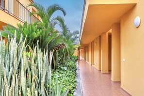 Un couloir bordé de plantes et un bâtiment jaune doté d’un sol carrelé.