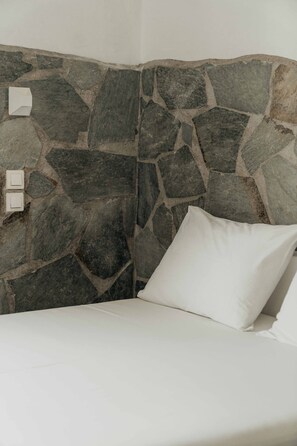 Rincón de una habitación con pared de piedra, un almohadón blanco y dos interruptores de luz.
