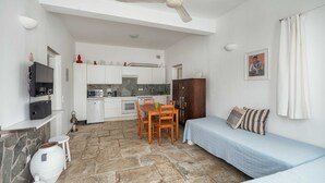 Ein gemütlicher Raum mit Küchenzeile, einem Esstisch mit Stühlen, einem Bett und einem Deckenventilator.