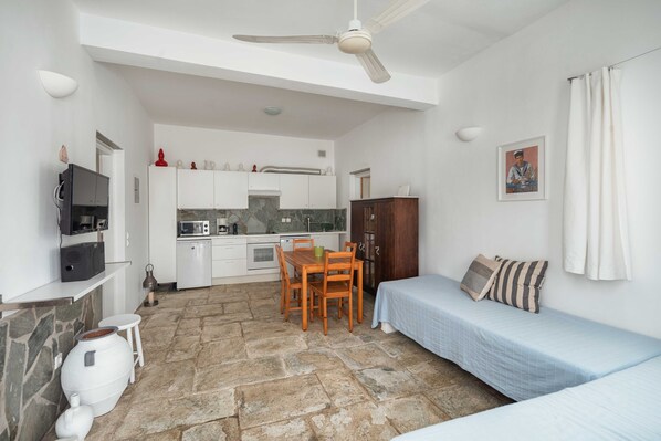 A compact room with a kitchenette, a dining table with chairs, a bed, and a ceiling fan.