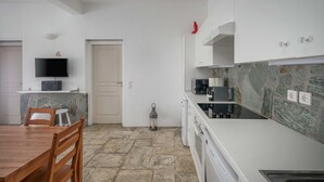 Eine moderne Küche mit Steinrückwand, weißen Schränken, einem Flachbildfernseher und einem Essbereich mit Holzsesseln.