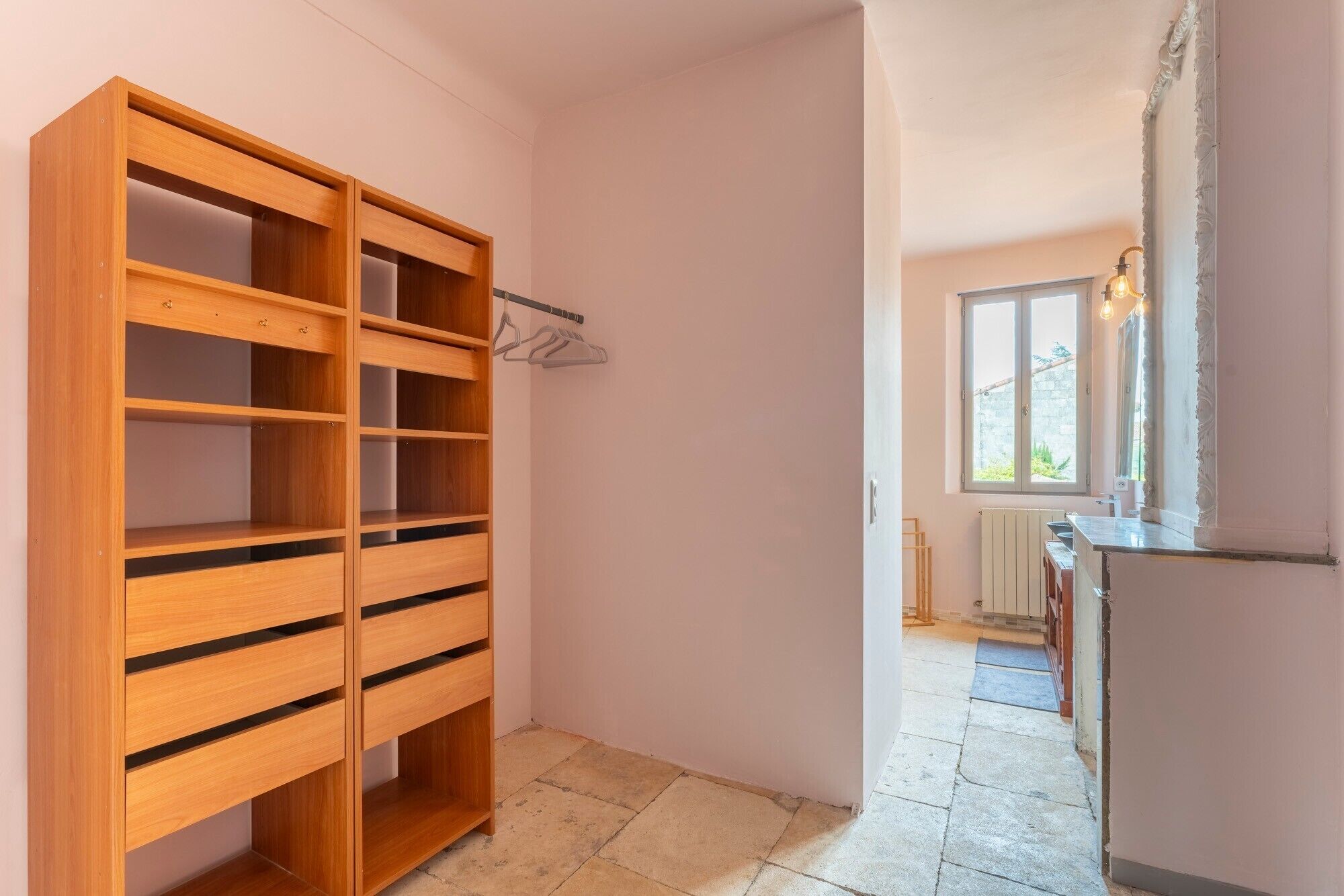 Un couloir avec une armoire en bois, un radiateur et une fenêtre donnant sur un paysage verdoyant.