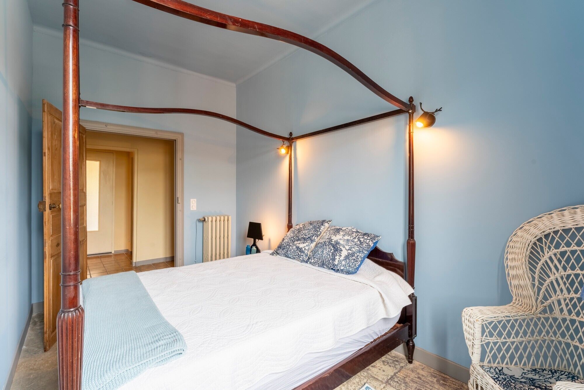 Una cama con dosel de madera, con un edredón blanco y almohadas estampadas.