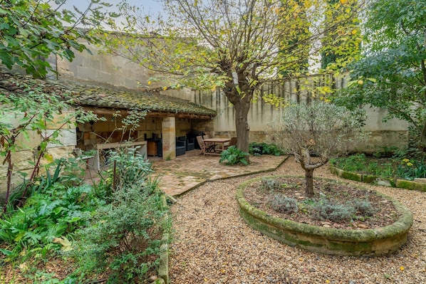 A courtyard with a stone table, a tree, and a stone wall.