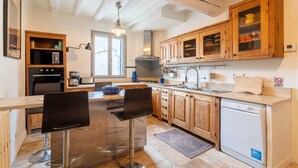 Cocina con armarios de madera, un refrigerador de acero inoxidable, un fregadero y una zona con taburetes de bar.