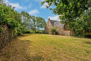 Une maison en pierre avec une cour verdoyante et des arbres.