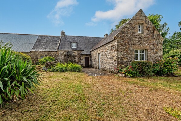 Une maison en pierre avec un toit en pente, une petite porte d’entrée et une fenêtre bien visible.