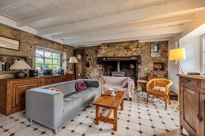 Une pièce chaleureuse avec un mur en pierre, une cheminée, un canapé, une table en bois et une chaise en osier.