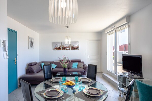 A modern living room with a sofa, a dining table set for four, a TV, and artwork on the walls.