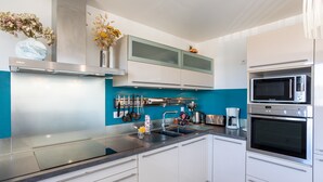 A modern kitchen with white cabinets, a stainless steel range hood, a double oven, and a blue accent wall. - Apartment 'Appart Villa Margaux Near the Sea' with Private Terrace and Wi-Fi (Les Sables-d'Olonne)