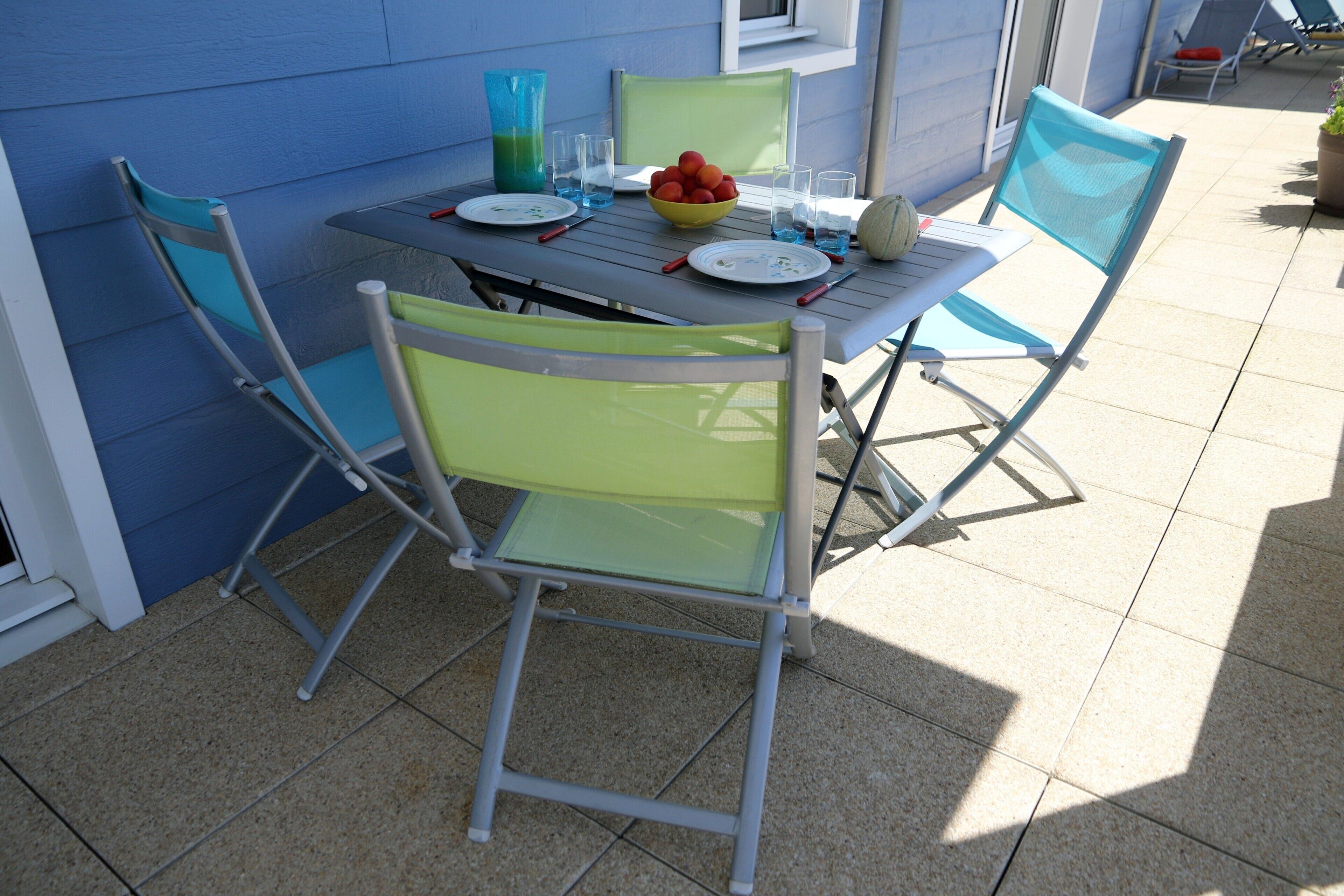 A patio table with chairs, a bowl of fruit, and a vase.