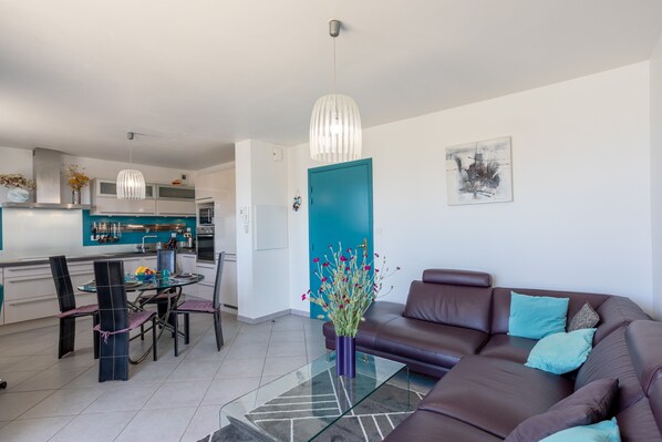 A modern living room with a glass coffee table, a brown leather sofa, and a teal door.
