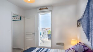 A bedroom with a bed, a window, a door, and a wall-mounted lamp. - Apartment 'Appart Villa Margaux Near the Sea' with Private Terrace and Wi-Fi (Les Sables-d'Olonne)