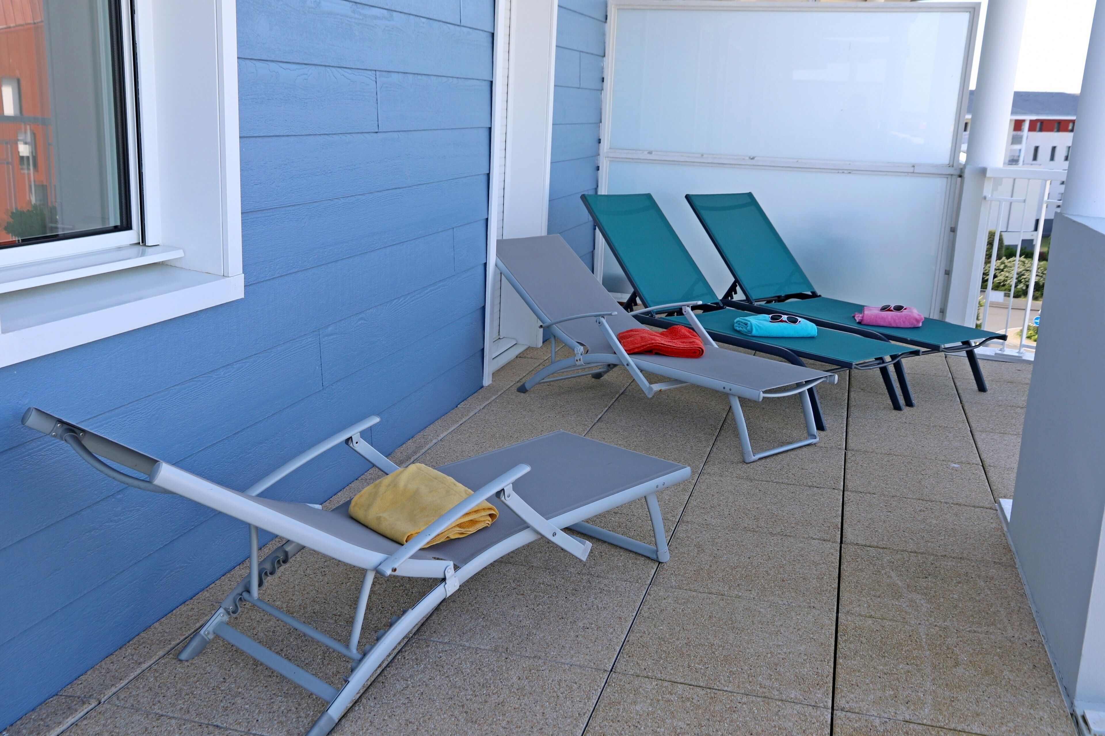 Un balcon avec deux chaises longues, l’une avec une serviette jaune et l’autre avec une serviette rose.
