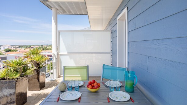 A balcony with a table set for two, a bowl of fruit, and a green chair. - Apartment 'Appart Villa Margaux Near the Sea' with Private Terrace and Wi-Fi (Les Sables-d'Olonne)