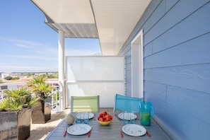 A balcony with a table set for two, a bowl of fruit, and a green chair.