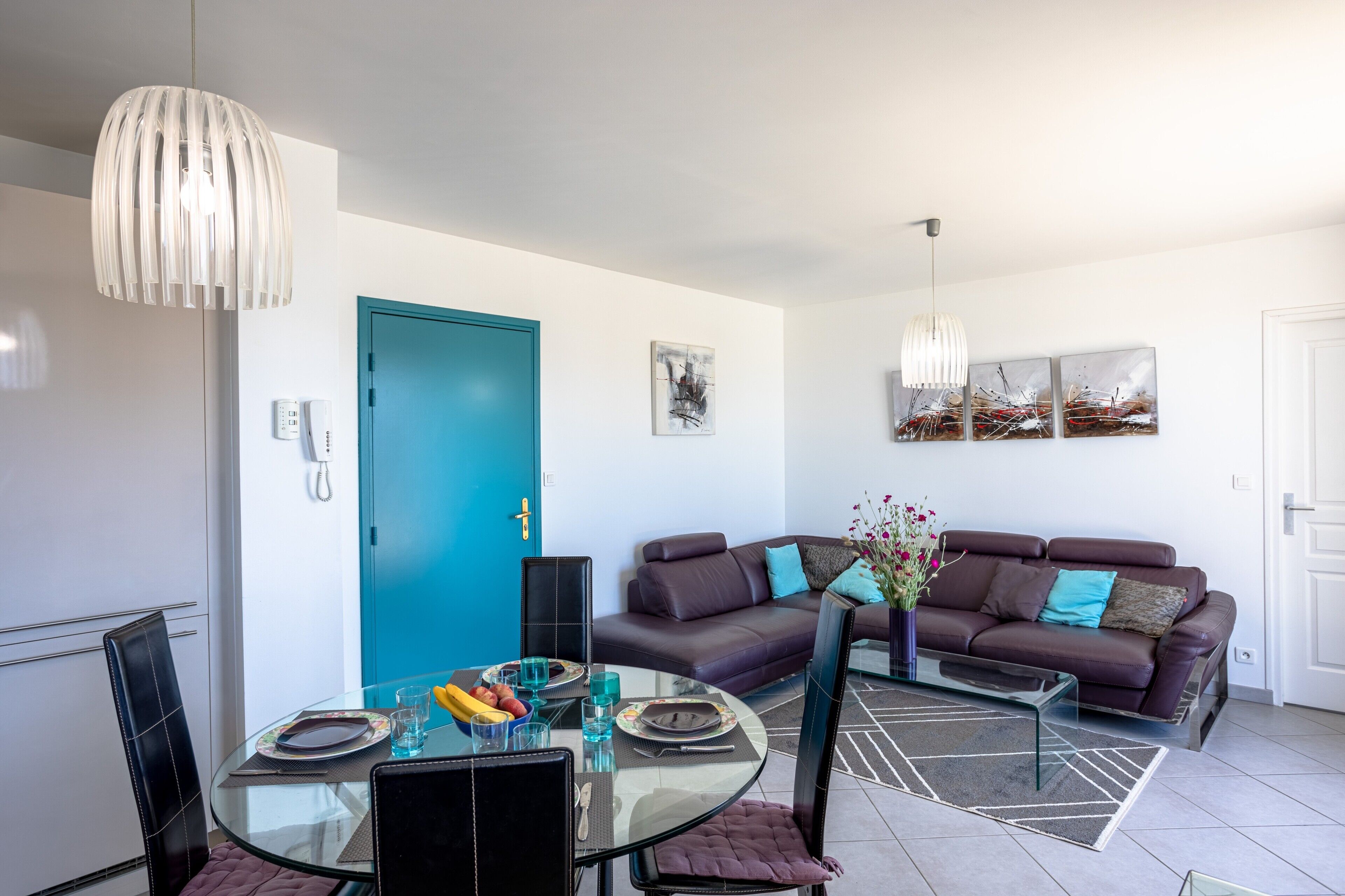 A modern living room with a glass dining table, a sofa, and a blue door.