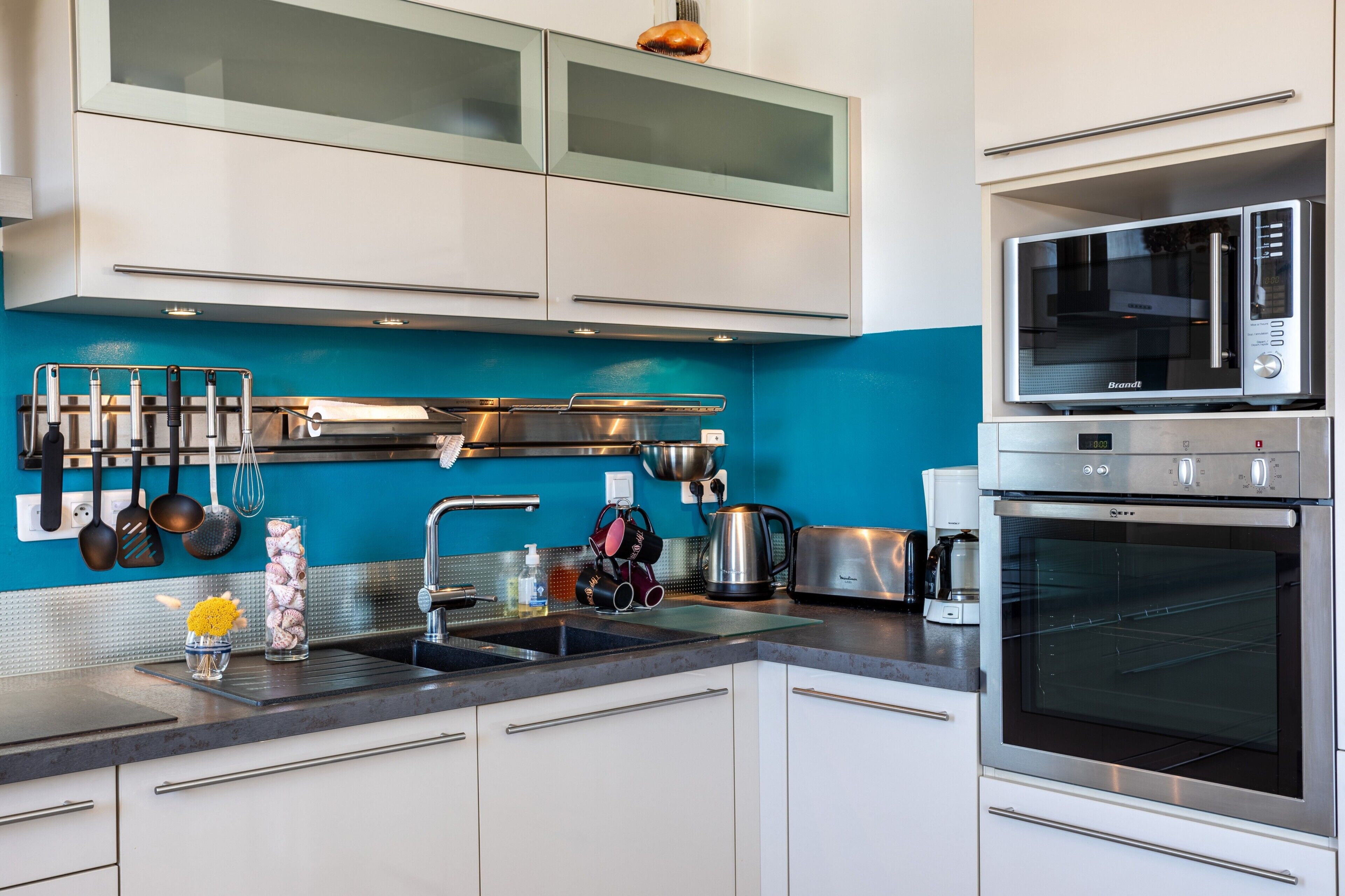 Eine moderne Küche mit Edelstahlgeräten, einer blauen Spritzschutzwand und weißen Schränken.