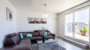 A modern living room with a sectional sofa, a glass coffee table, and artwork on the wall. - Apartment 'Appart Villa Margaux Near the Sea' with Private Terrace and Wi-Fi (Les Sables-d'Olonne)