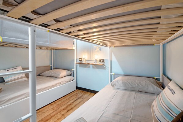 A bunk bed room with a wooden ceiling, a nightstand with a lamp, and a wall-mounted shelf.