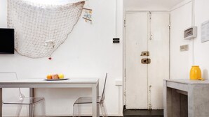 A room with a white door, a table with a fruit plate, clear chairs, a hanging net, and a yellow object on a table. - Apartment 'Baia Del Silenzio Beach' with Wi-Fi and Air Conditioning (Sestri Levante)