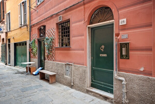 A narrow street with a red building featuring a green door, a bench, and a small table.