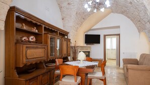A dining area with a wooden table, chairs, and a cabinet. There is a television mounted on the wall and a sofa in the living area. - Apartment 'La Dimora In Ostuni' with Air Conditioning (Ostuni)
