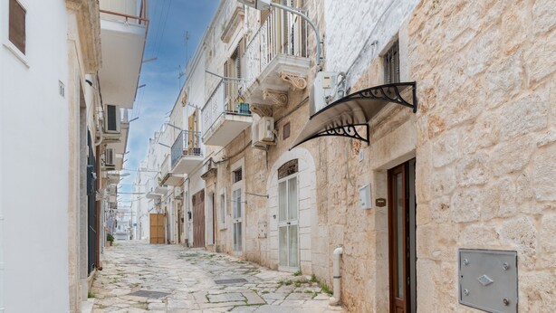 A narrow cobblestone street flanked by buildings with balconies, a metal awning, and a door. - Apartment 'La Dimora In Ostuni' with Air Conditioning (Ostuni)