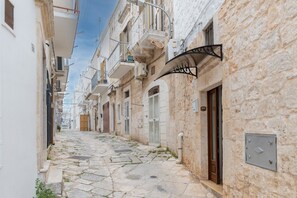 A narrow cobblestone street flanked by buildings with balconies, a metal awning, and a door. - Apartment 'La Dimora In Ostuni' with Air Conditioning (Ostuni)