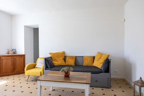 Uma sala de estar com sofá, poltrona amarela, mesa de centro de madeira e um armário.