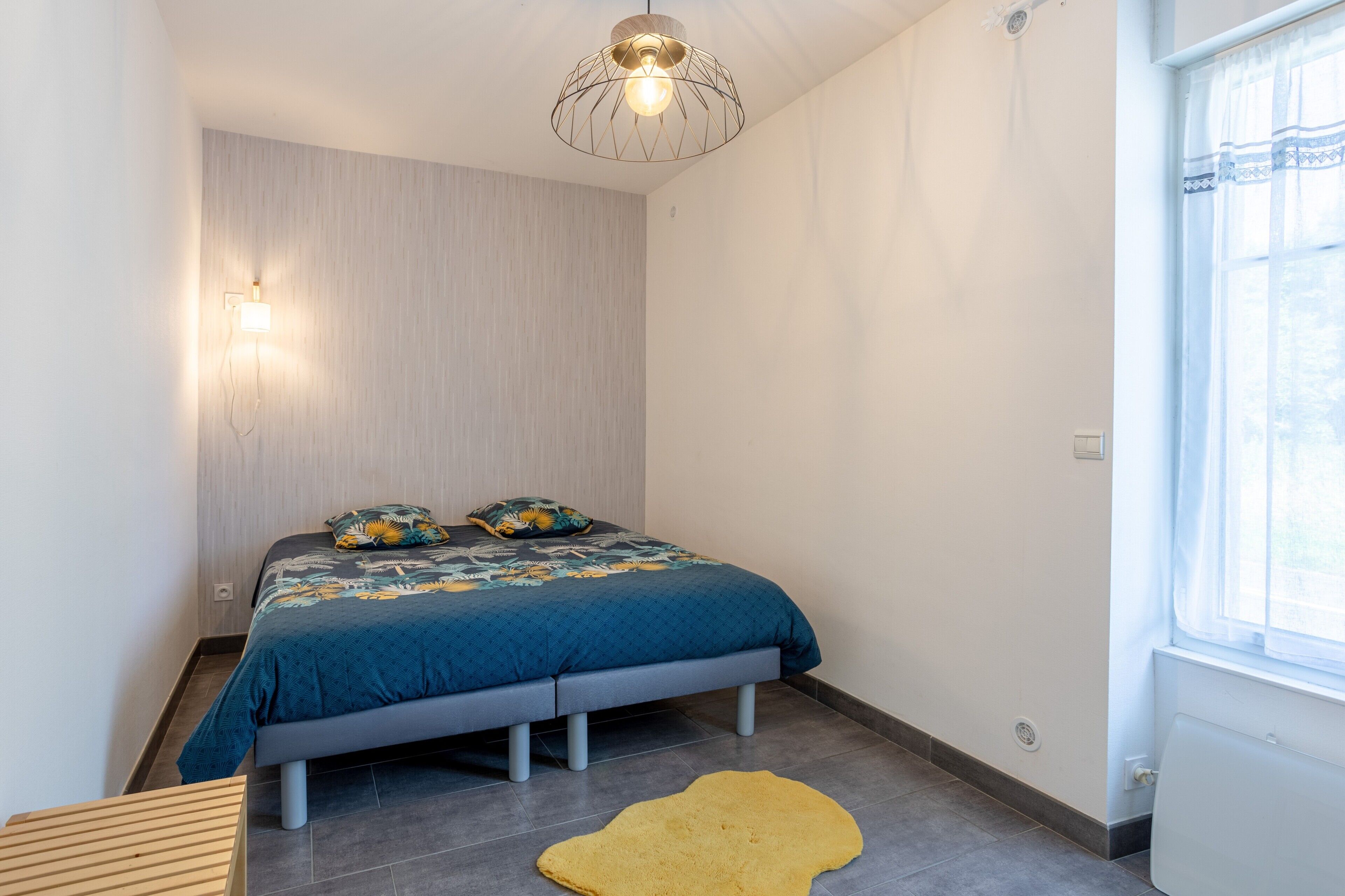 A bedroom with a bed, a wall-mounted light, a window, and a radiator.