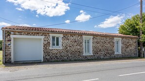 Un edificio de dos pisos de piedra con techo de tejas, una puerta de garaje y dos ventanas.