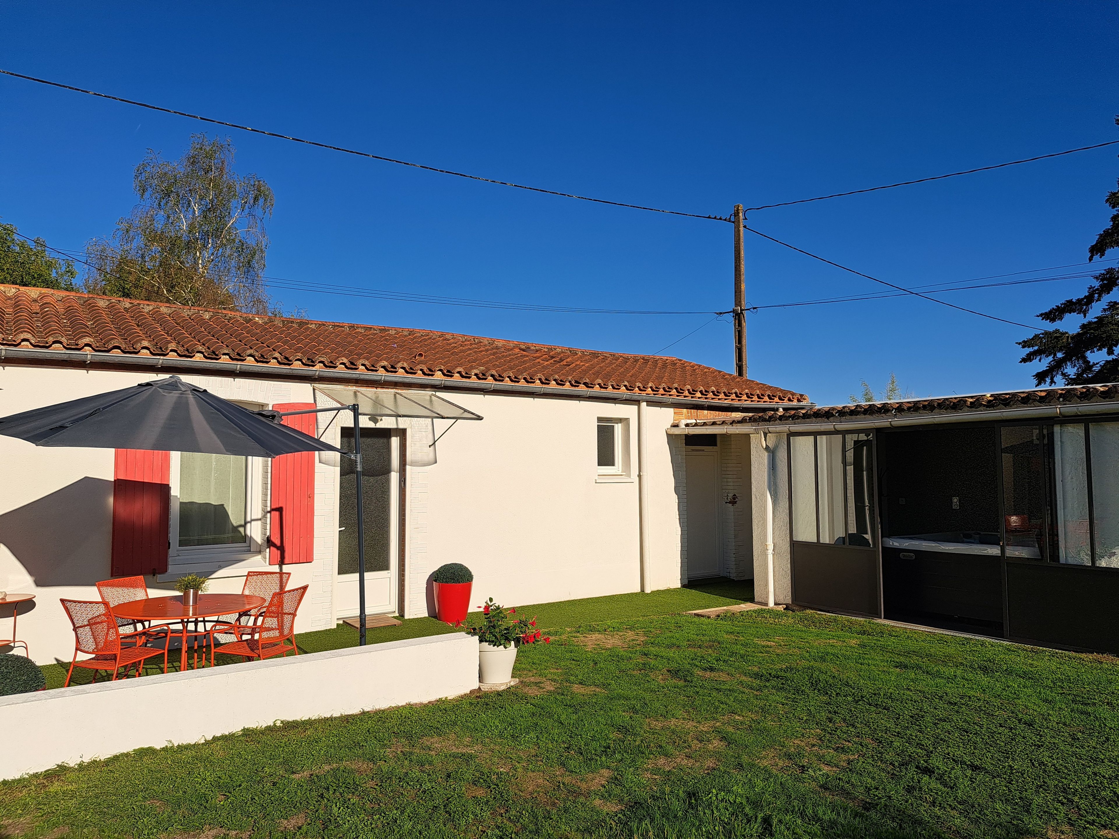 Ein Haus mit Terrasse, einem Esstisch mit Stühlen, einer roten Tür und einem überdachten Außenbereich.
