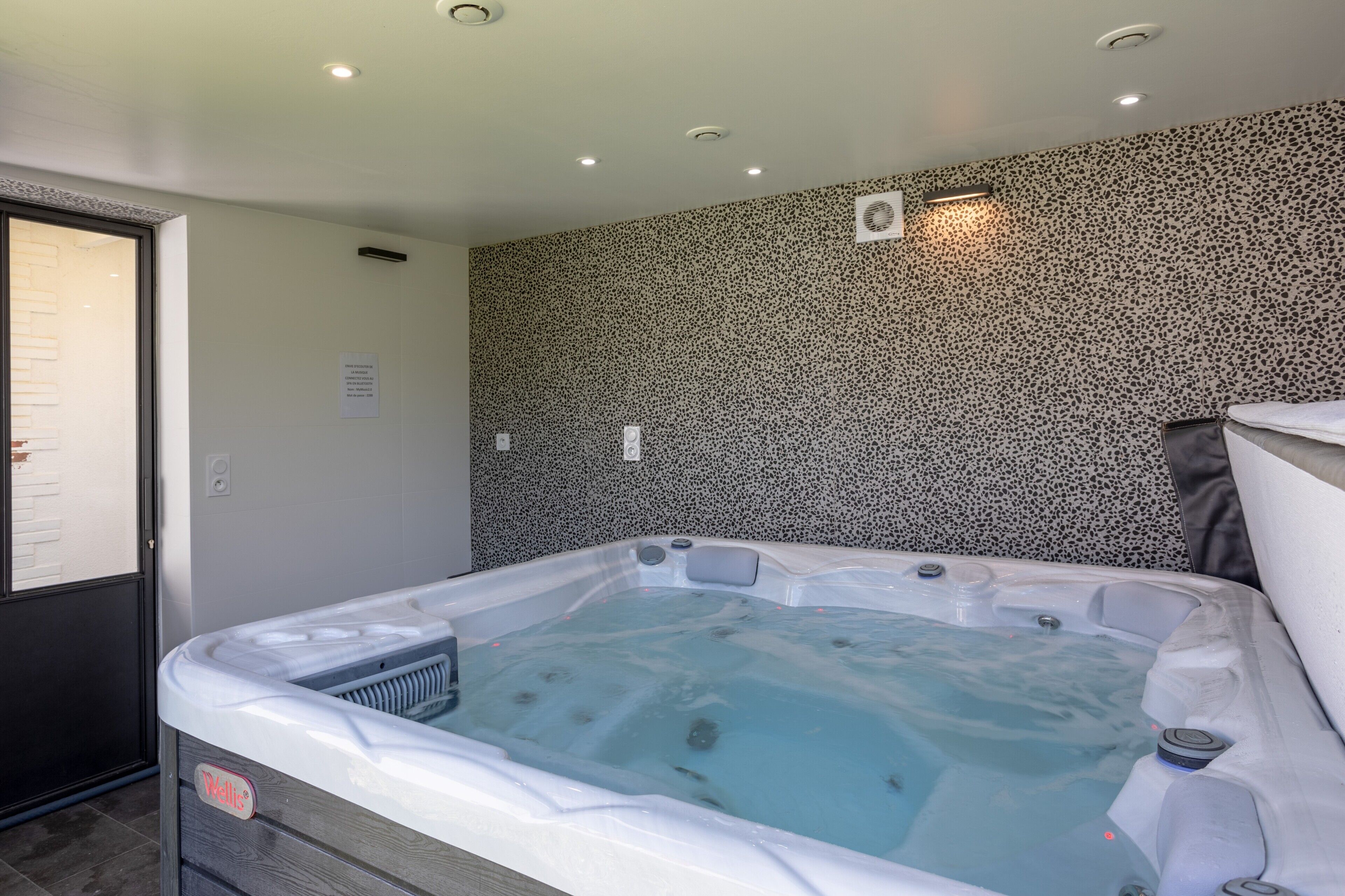 Un bain à remous dans une pièce dont le mur est recouvert d’un motif moucheté et où se trouve une porte sur le côté gauche.