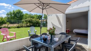 Un patio al aire libre con mesa, sillas, un paraguas grande y vistas a un jardín.