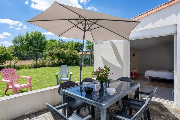 Terrassa exterior amb taula, cadires, un parasol gran i vistes al jardí.