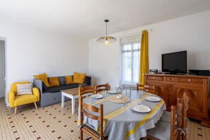 Uma sala de jantar com uma mesa posta para quatro pessoas, um sofá, uma televisão e um armário.