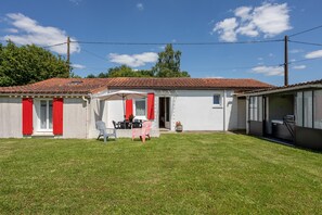 Una casa amb teulada vermella, un petit pati amb taula i cadires, i un jardí amb gespa.