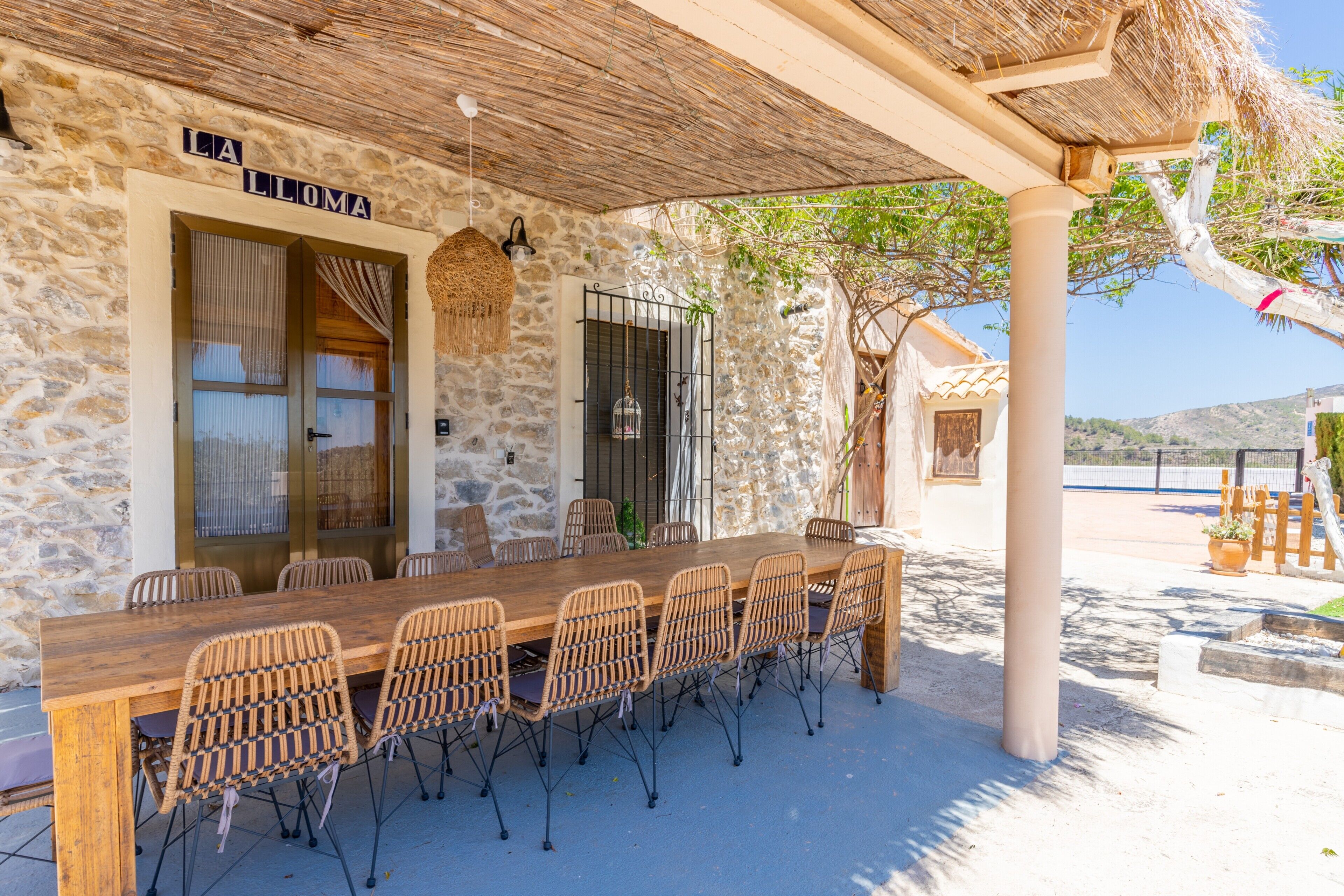 Un bâtiment en pierre avec une table en bois et des chaises en osier, une enseigne indiquant « LA LOMA », et un toit de chaume.