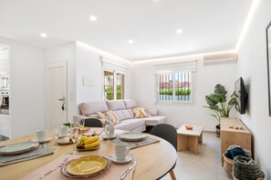 Un salon moderne avec un coin repas, des murs blancs et une grande fenêtre donnant sur un paysage verdoyant.