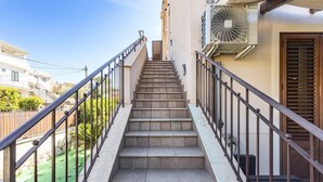 Un escalier menant à l’entrée d’un bâtiment, avec une rampe en métal, un ventilateur et une porte dotée d’une fenêtre.