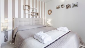 Une chambre d’hôtel avec un mur à rayures, un lit avec une tête de lit, des tables de chevet avec des lampes et des œuvres d’art accrochées au mur.