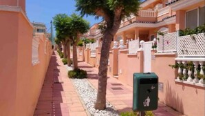 Una calle residencial con casas similares, cielo despejado y un contenedor de basura.