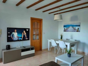 Un soggiorno con TV, una porta in legno, un'area pranzo con sedie, un tavolo e un quadro appeso al muro.