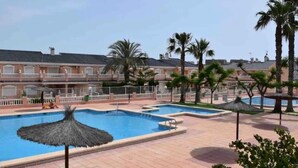 Un área de piscina con varias piscinas, palmeras y un edificio con balcones.
