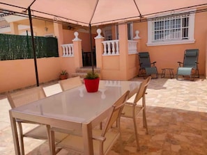 Un patio coperto con tavolo e sedie, una pianta in vaso e una finestra con grate bianche.