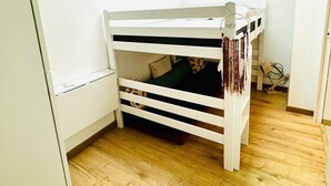 A bedroom with a bunk bed, wooden flooring, a skylight, and a white wall.