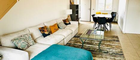 Ein Wohnzimmer mit Sofa, Couchtisch, Esstisch mit Stühlen, einer Treppe und einer Tür zu einem anderen Raum.