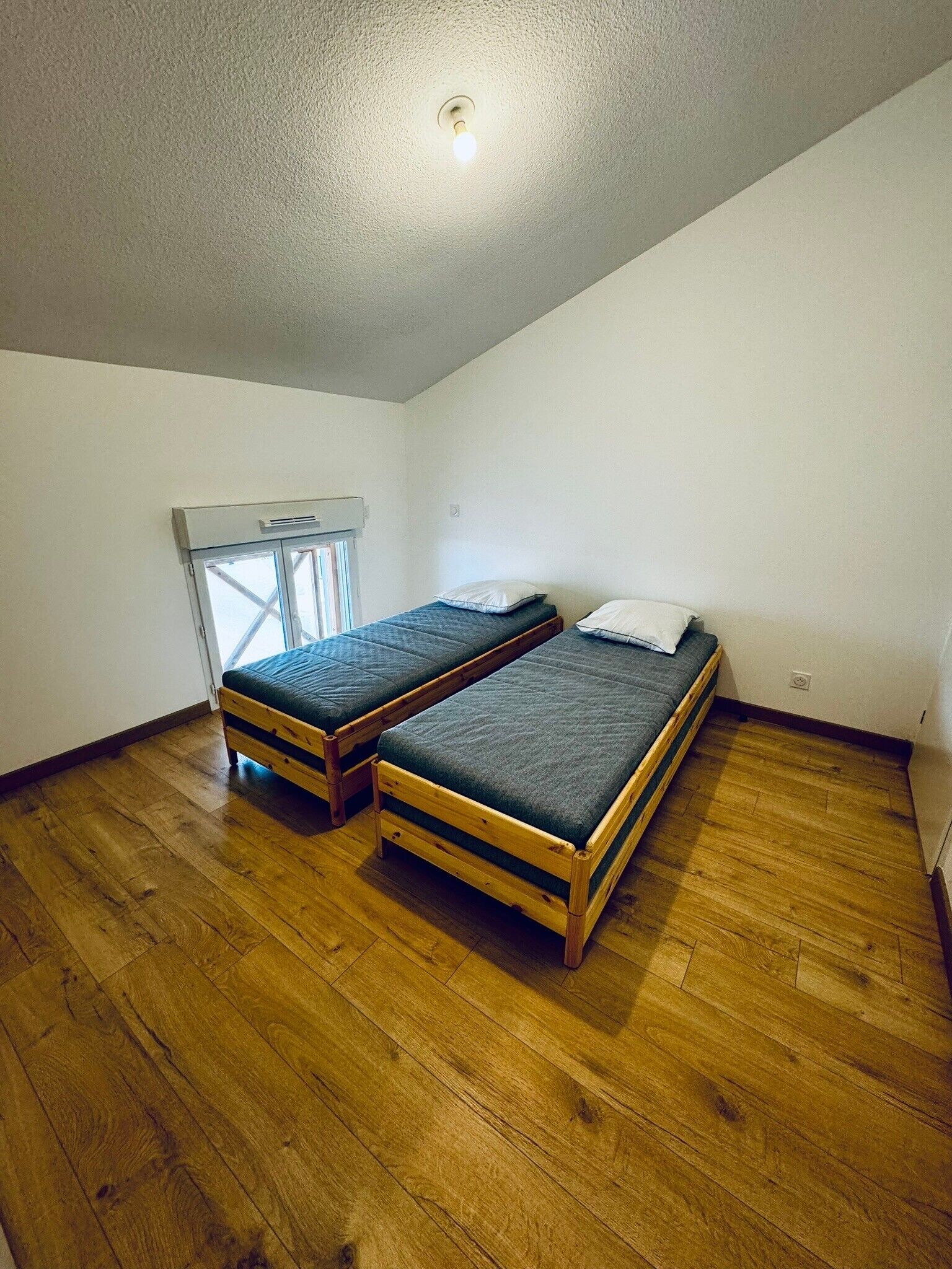 A room with two wooden beds, a window with blinds, and a ceiling light.